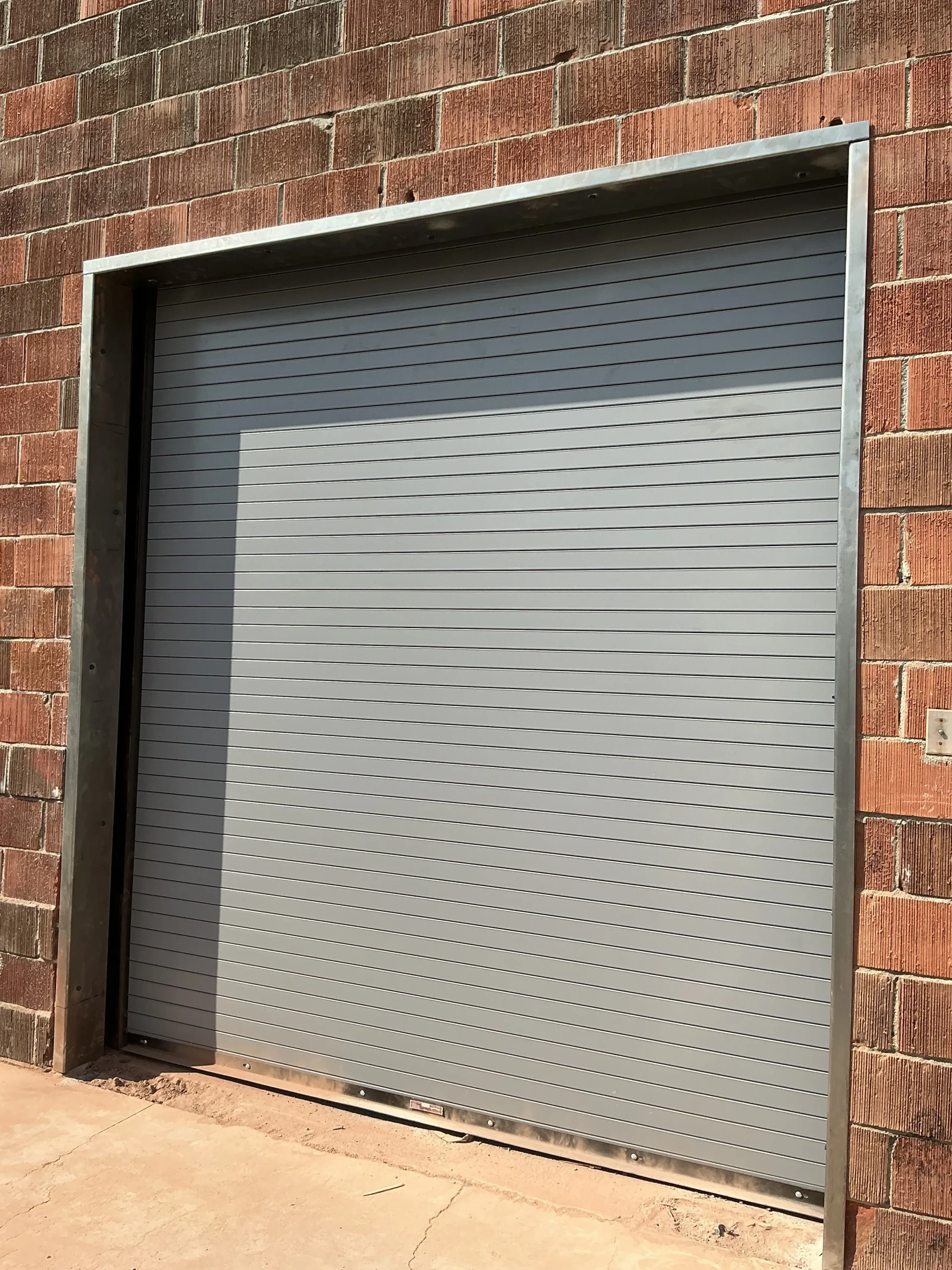 A heavy-duty gray rolling steel shutter door installed on a brick commercial building, showing the work of a professional overhead door company in Torrance, CA.