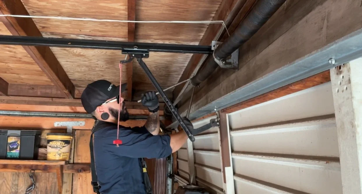 A technician working under a wooden ceiling to fix the overhead torsion system, demonstrating a broken garage door spring repair.