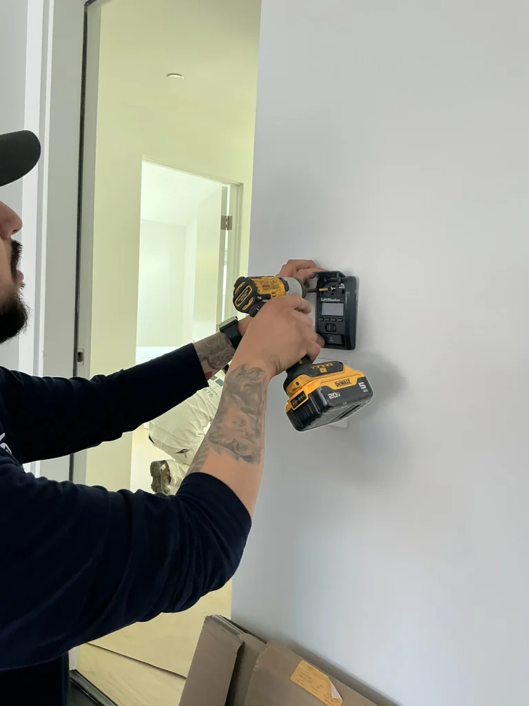 A technician using a power drill to mount a smart LiftMaster wall control panel, demonstrating essential garage door security tips.