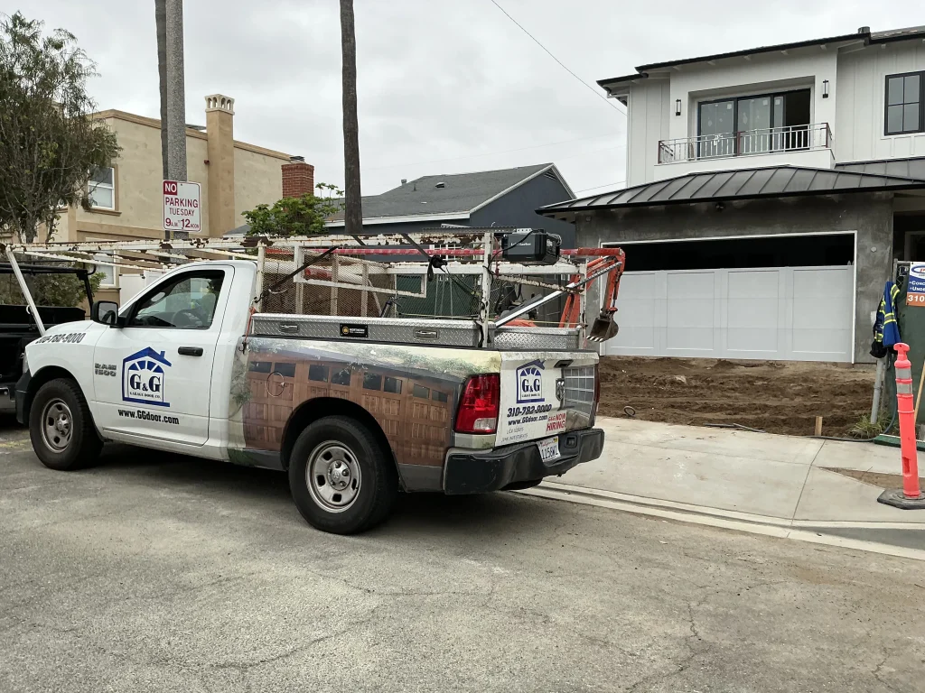 A white service truck parked on the street during a professional 16x8 garage door installation at a residential home construction site.