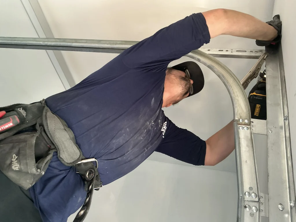 A technician with a tool belt adjusting a curved metal track panel to fix a garage door off track problem.