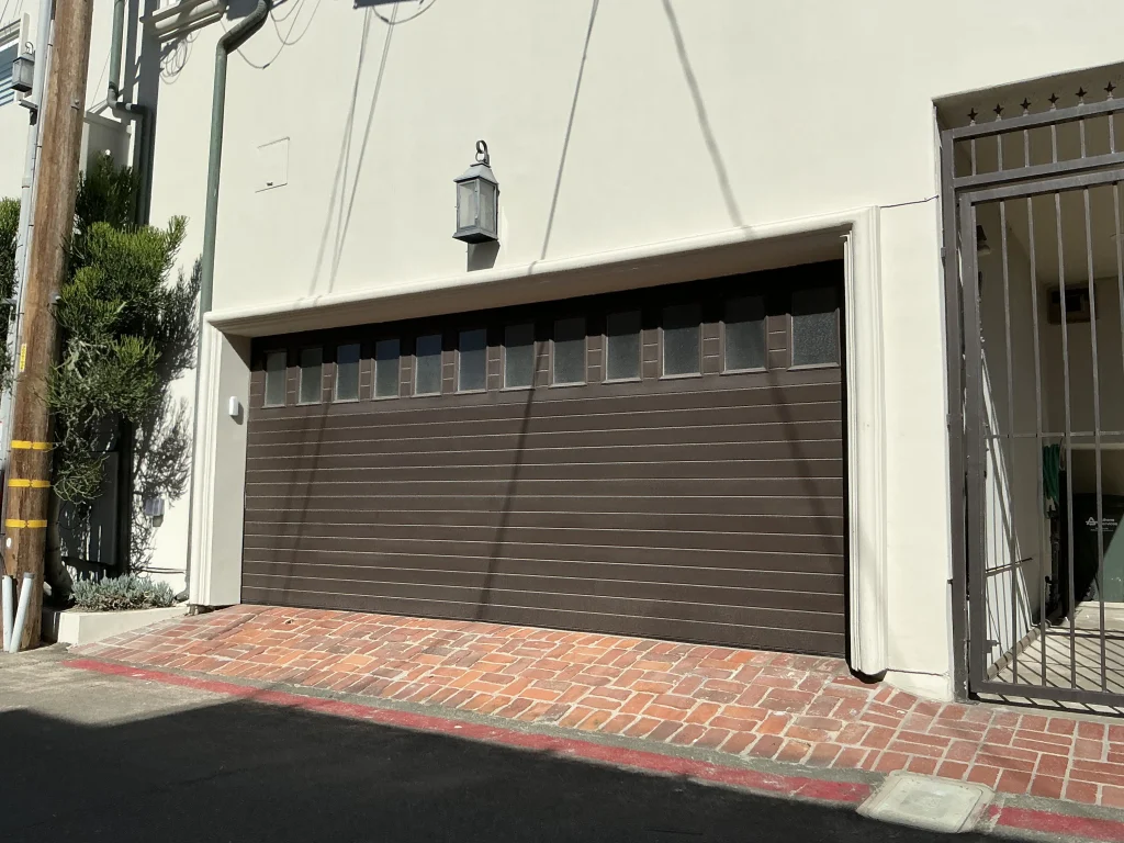 A dark brown horizontal panel garage door with a top row of frosted windows installed on a stucco home, showcasing various types of 16x8 garage doors.
