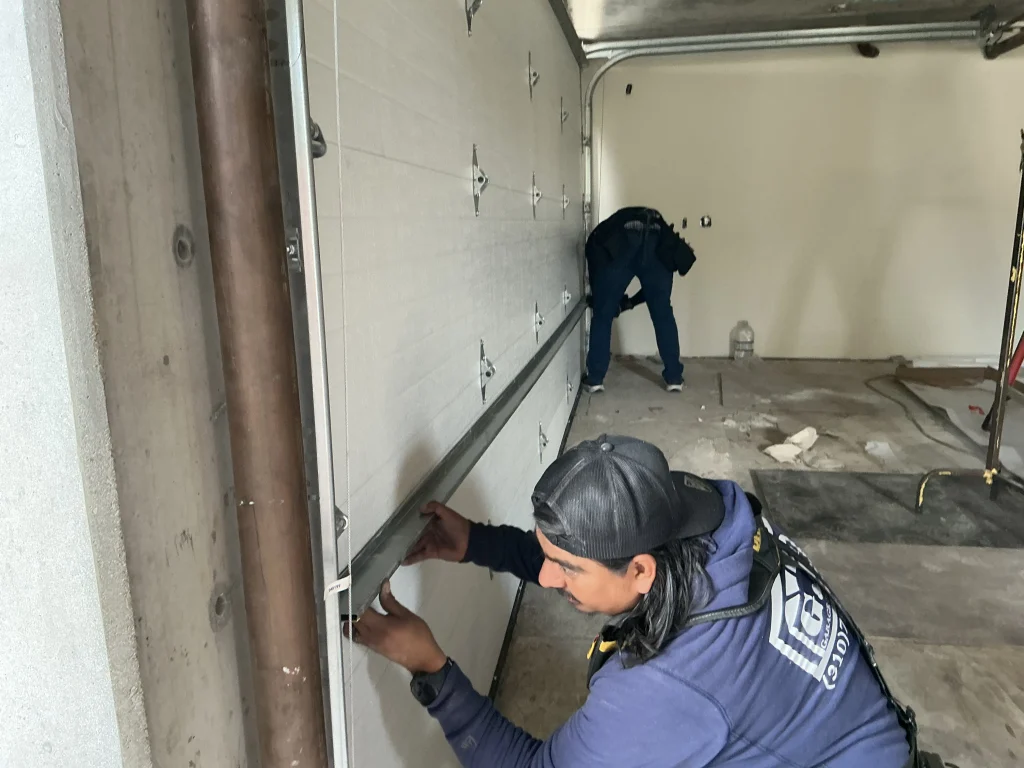A technician precisely aligning a white panel door section inside a garage, illustrating why they are considered the best garage door company in Torrance, CA.