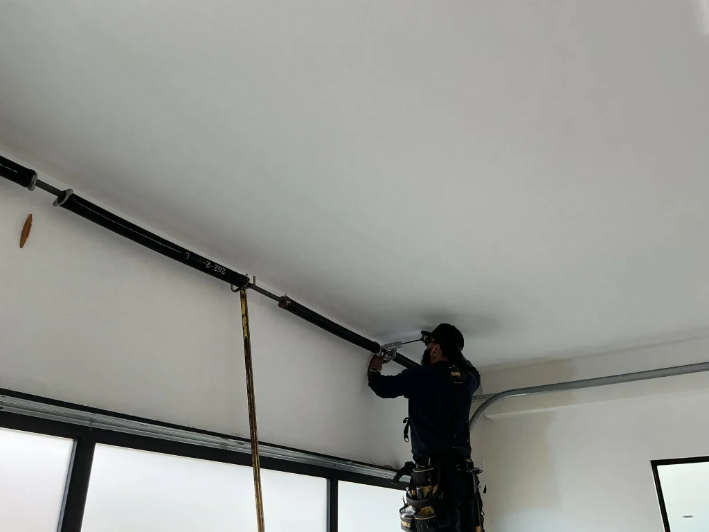 A technician working on a torsion spring system above a modern glass door, performing a professional garage door spring replacement in Torrance, CA.