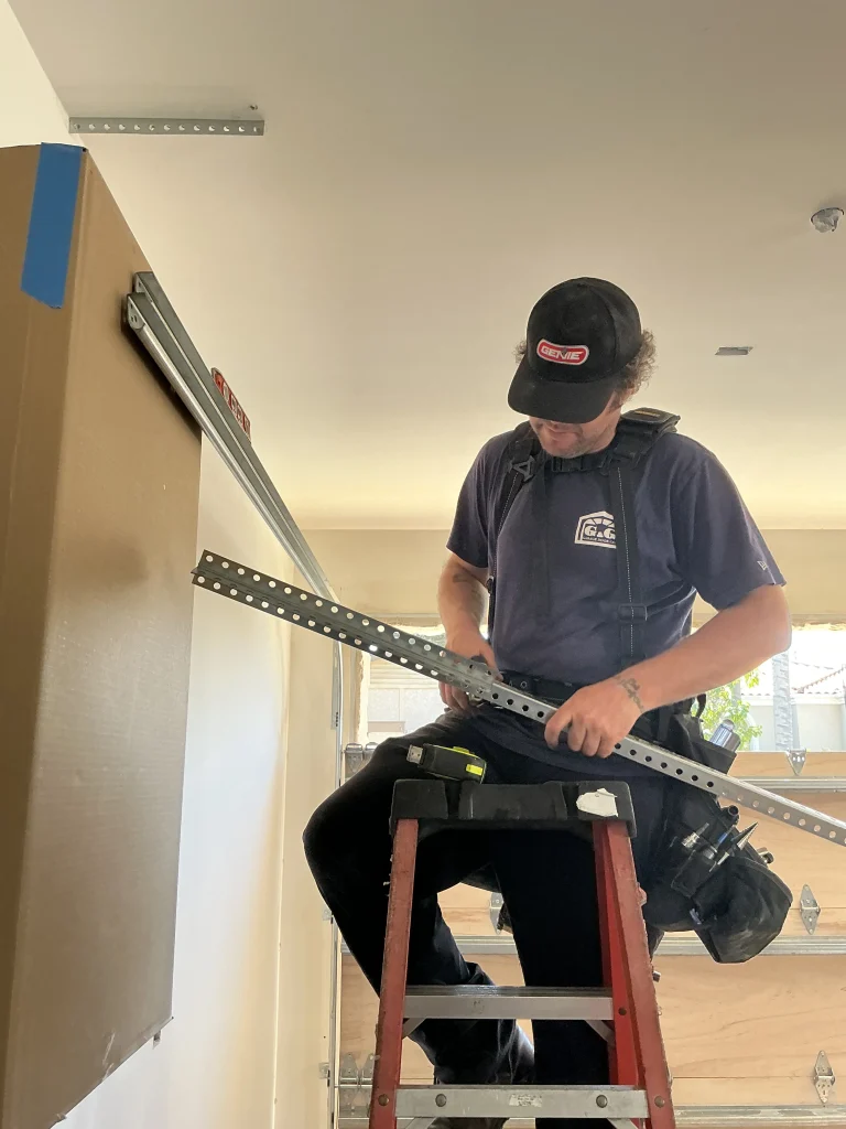 A technician on a ladder adjusting structural hardware components, illustrating the steps on how to maintain your garage door.