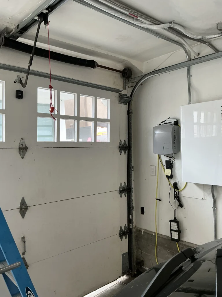 An interior view of a white garage door showing the upper torsion spring assembly and tracks, illustrating the setup for a professional garage door spring replacement.