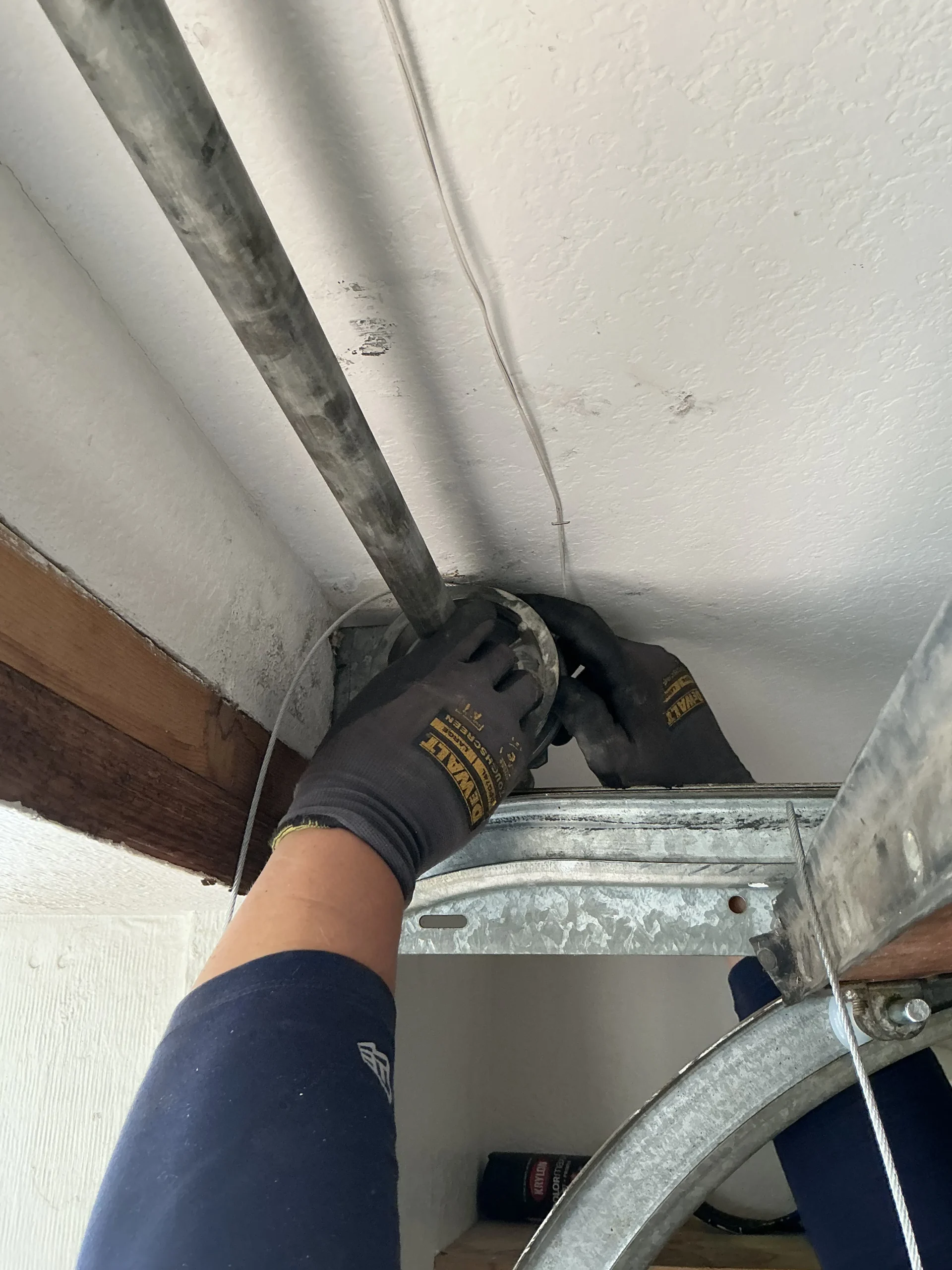 Gloved hands adjusting the upper cable drum and shaft assembly near the ceiling, illustrating practical maintenance tips for door track and backhangs.