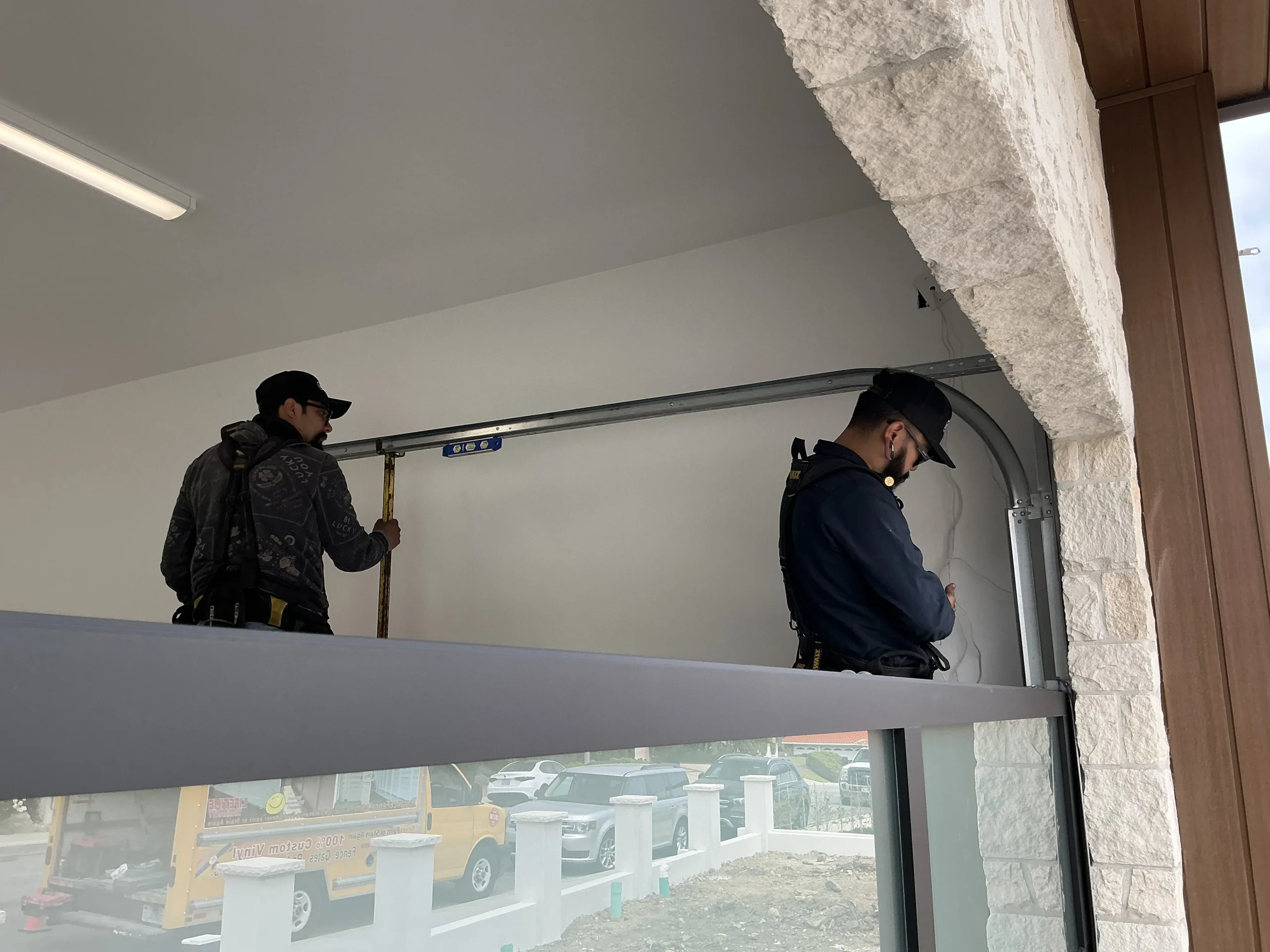 Two technicians using a level to precisely install and align one of the common types of overhead door track systems.