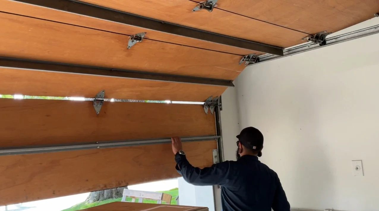 A technician inspection of an off-track wood-look section overhead system, showing the essential troubleshooting steps involved prior to a garage door roller replacement.