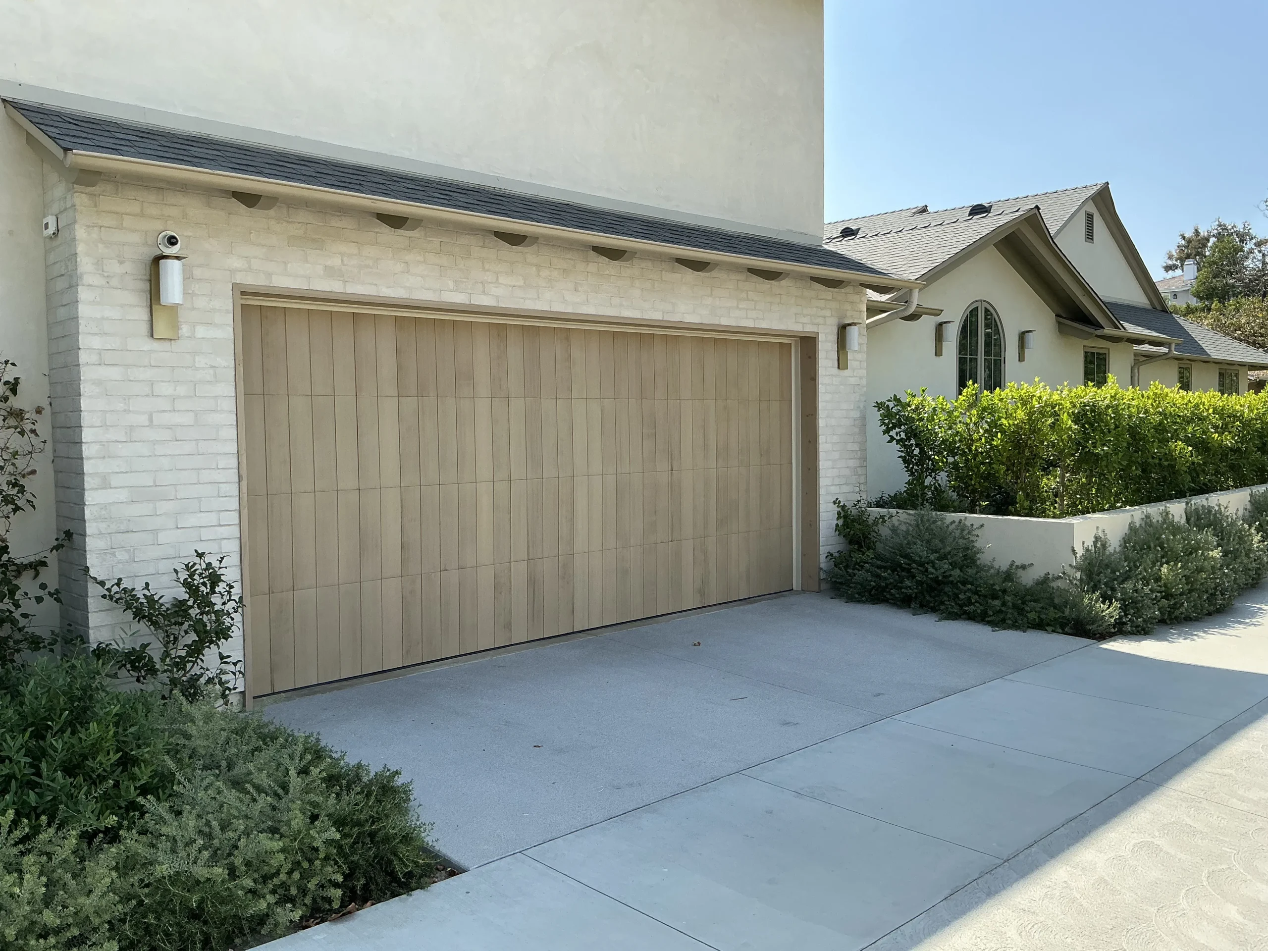 An exterior view of a modern home with a vertical wood-plank door and a visible security camera, showcasing an integrated system for garage door security.