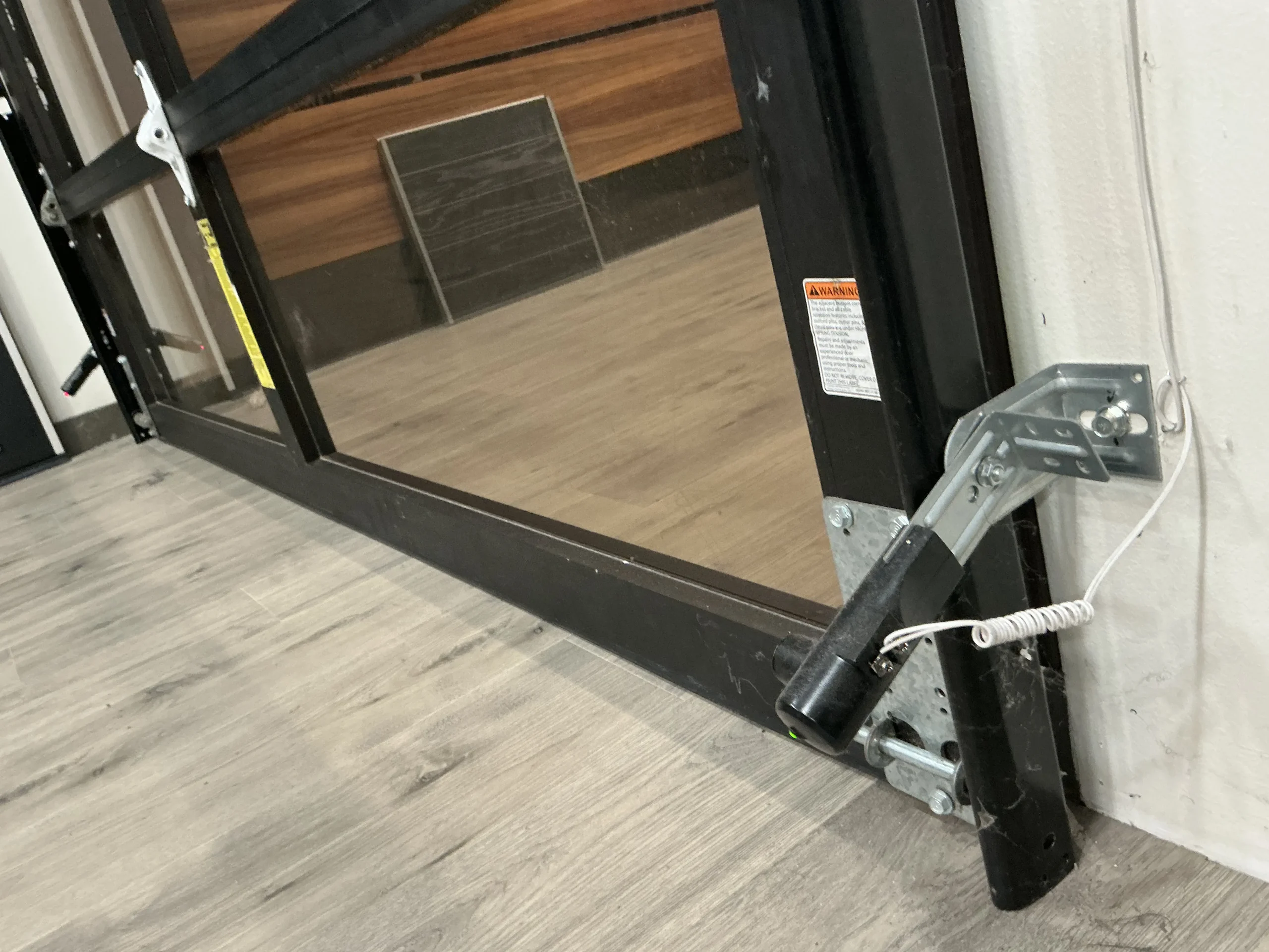 A safety photo-eye sensor mounted on a metal bracket at the bottom of a black garage door frame, demonstrating the setup of garage door sensors in Torrance, CA.
