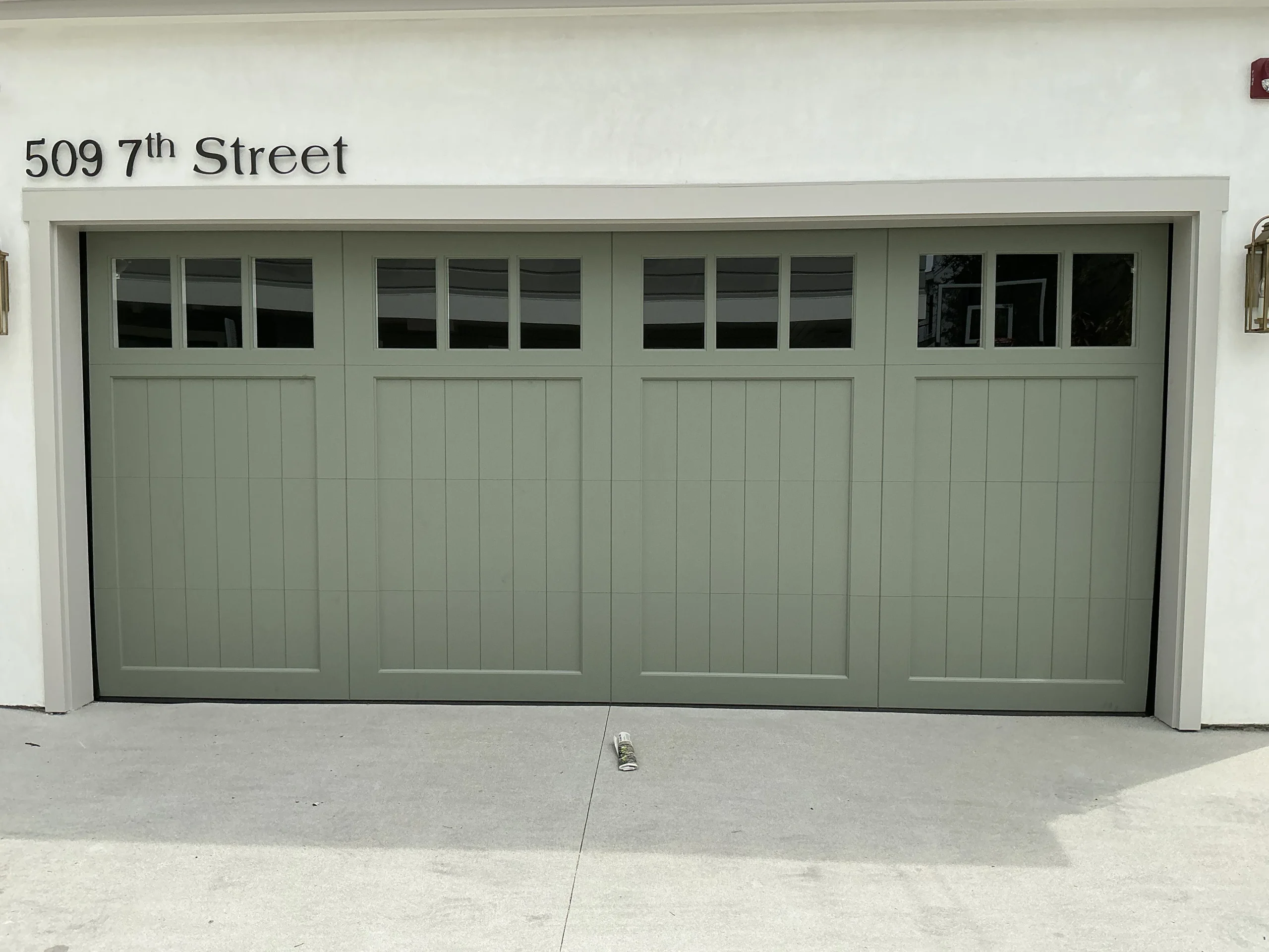 A beautiful sage-green carriage-style garage door with tinted upper windows, demonstrating how to maintain privacy and secure windows on your garage door.