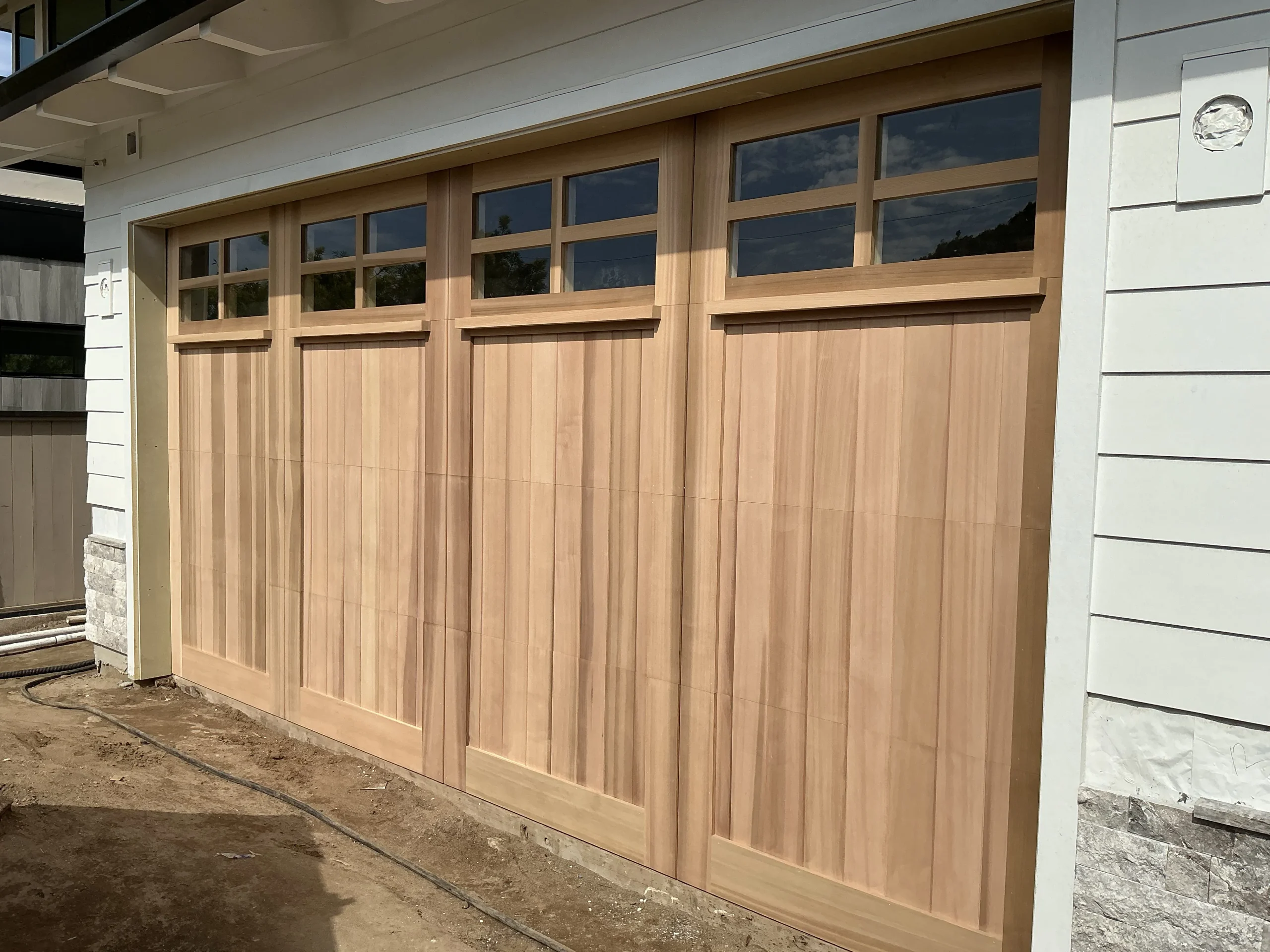 A beautiful, light-toned natural wood carriage-style garage door installed on a house, highlighting the aesthetic value and wooden garage door benefits.