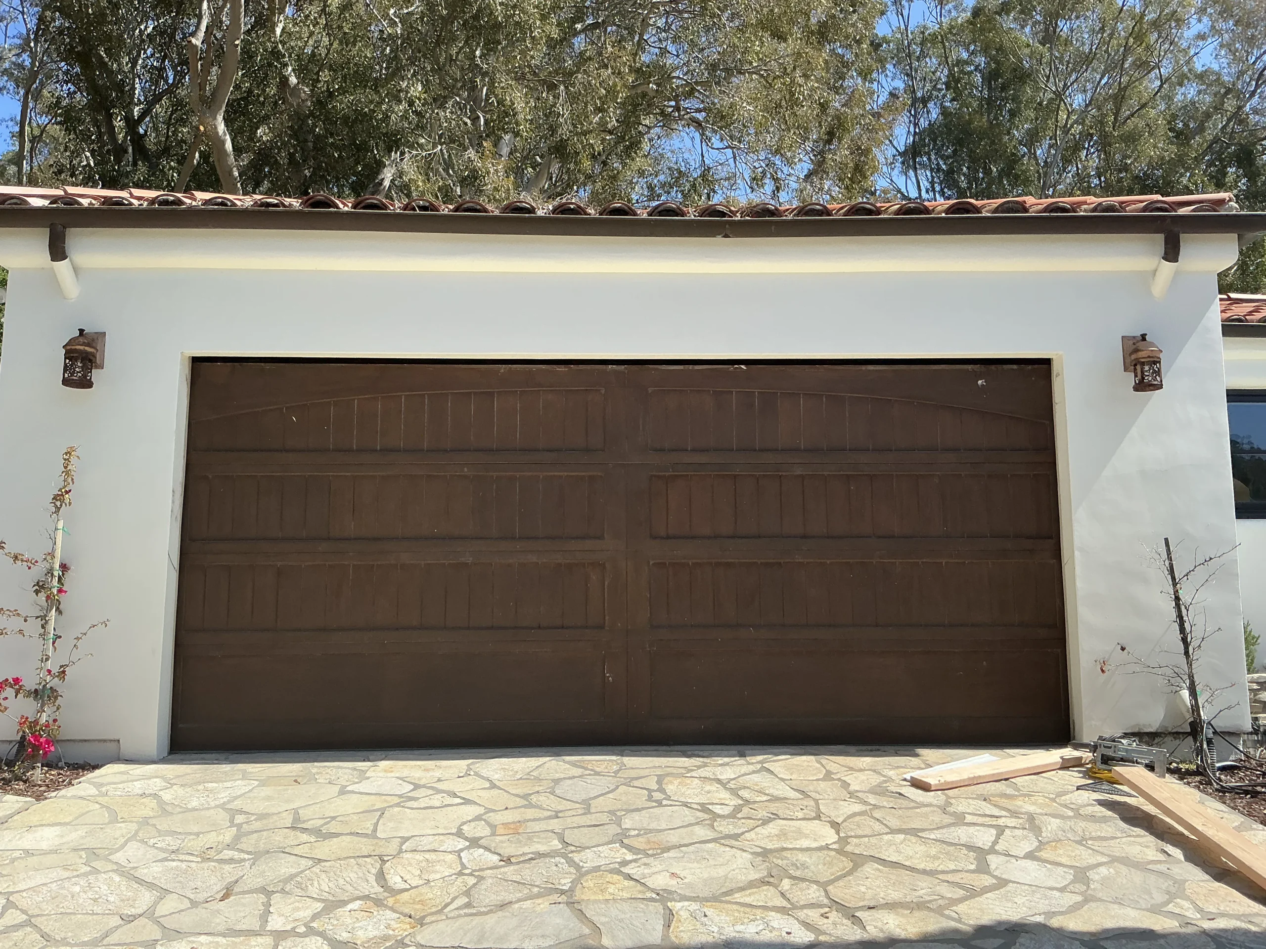 A wide dark-brown timber sectional door newly mounted on a Spanish-style stucco garage, showcasing a completed wooden garage door installation.