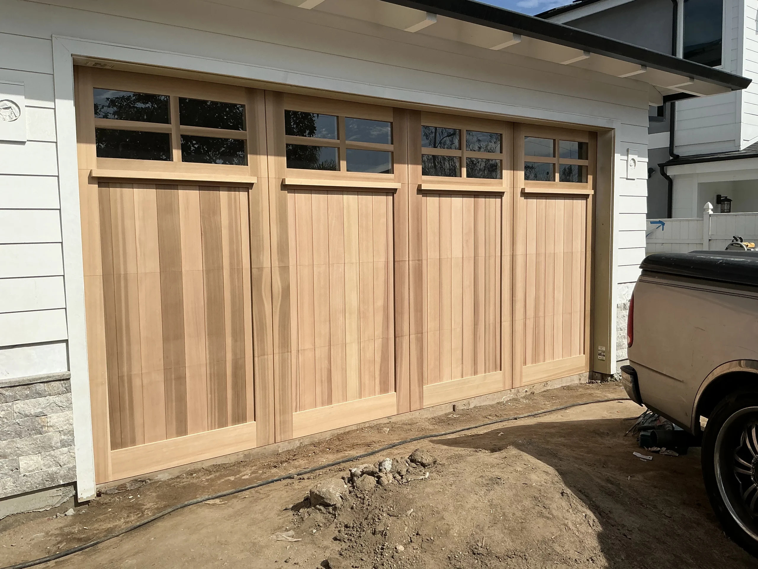 A beautiful, newly installed natural timber carriage-style door with upper glass windows, showcasing custom wooden garage doors in Torrance, CA.