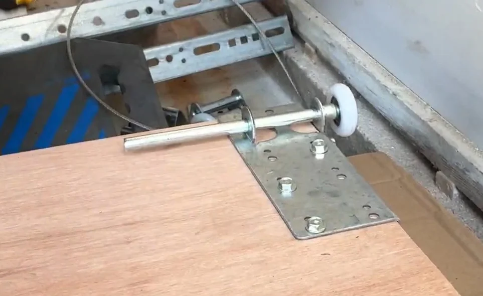 A close-up view of a new white nylon garage door roller assembled into a steel hinge fixture on a wood panel, ready to replace a worn garage door roller in Torrance, CA.