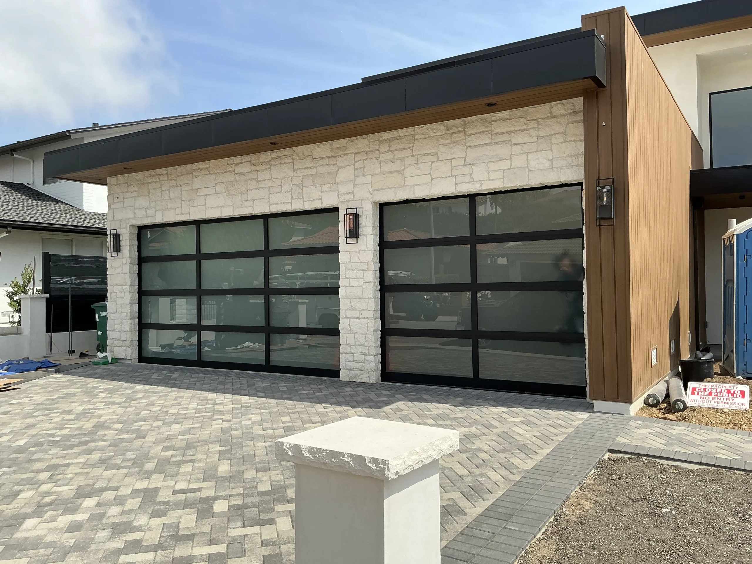 Two modern black-framed glass sectional garage doors installed on a contemporary stone and wood-sided home, highlighting stylish options for 9x8 garage door designs.