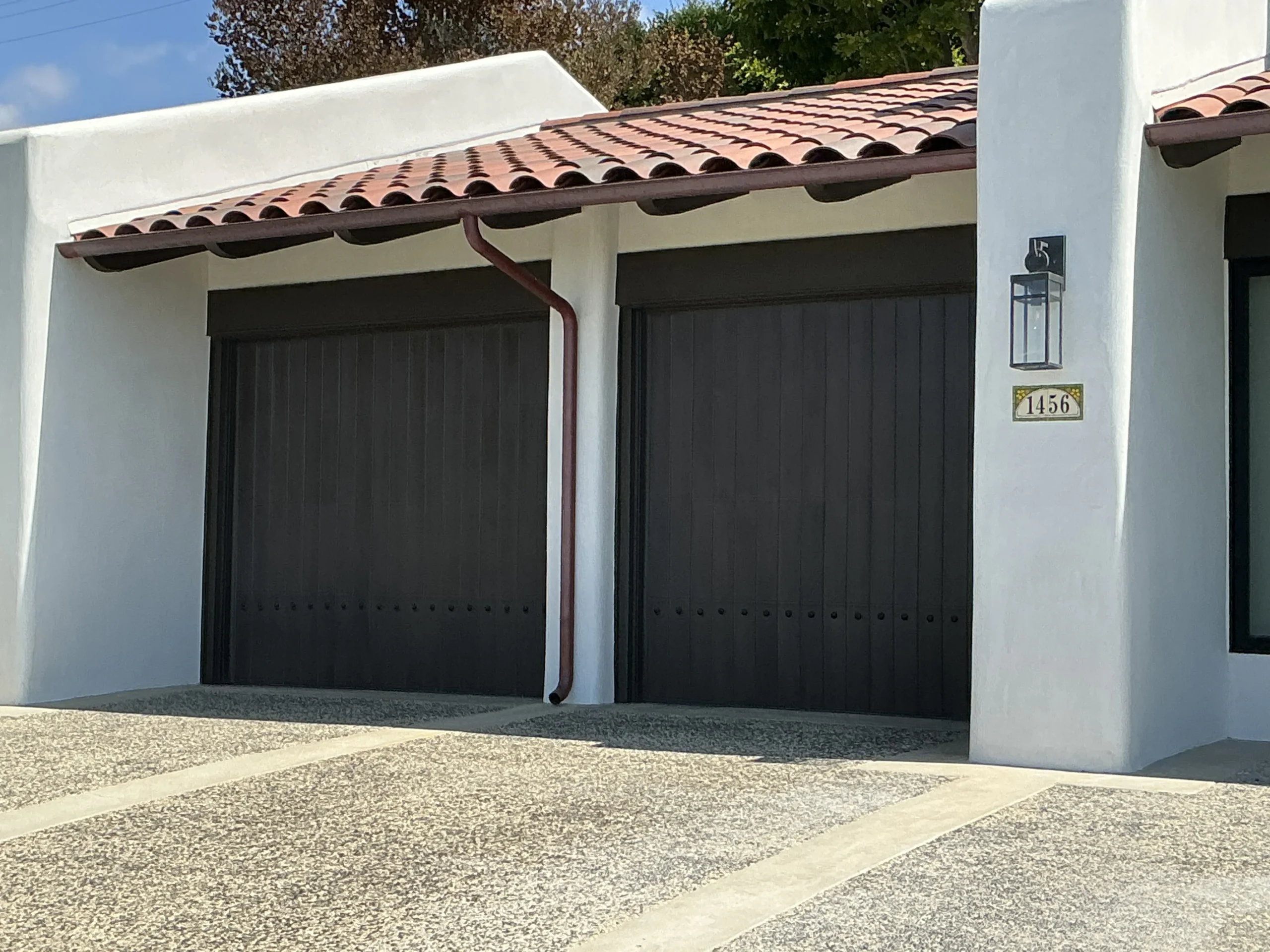 Two dark brown vertical-plank single car garage doors installed on a beautiful Spanish-style stucco home, showcasing a classic setup of 9x8 garage doors in Torrance, CA.