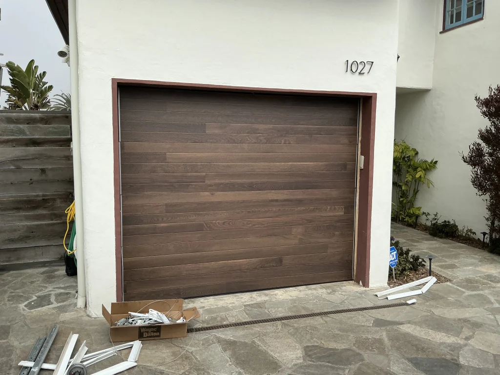 A dark horizontal wood-plank single car sectional door newly fitted into a residential stucco opening, showcasing a standard size setup for 9x8 garage doors.