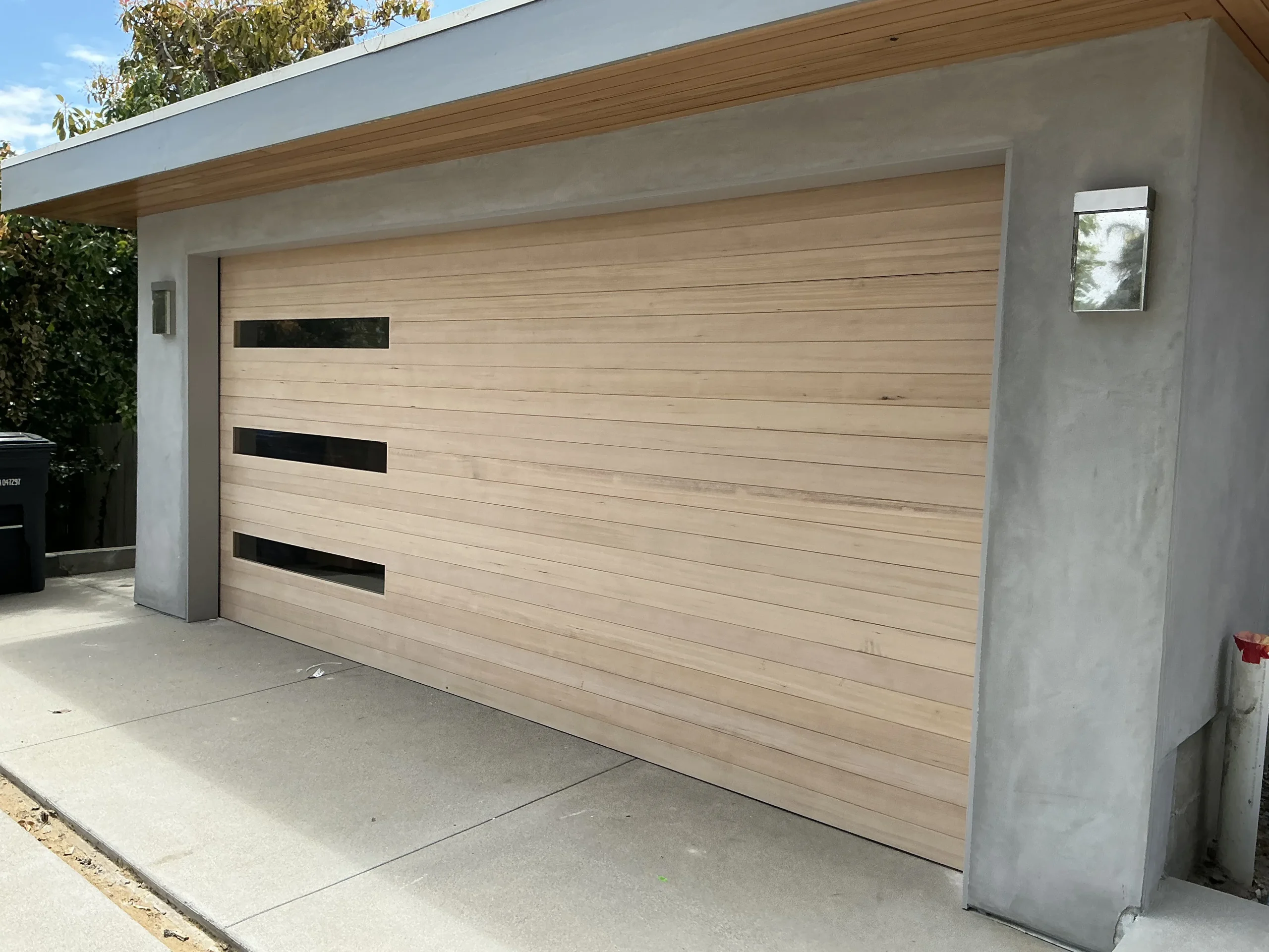 A modern, light-colored horizontal wood-plank garage door featuring three stacked side windows, demonstrating one of the best overhead garage doors for your home.