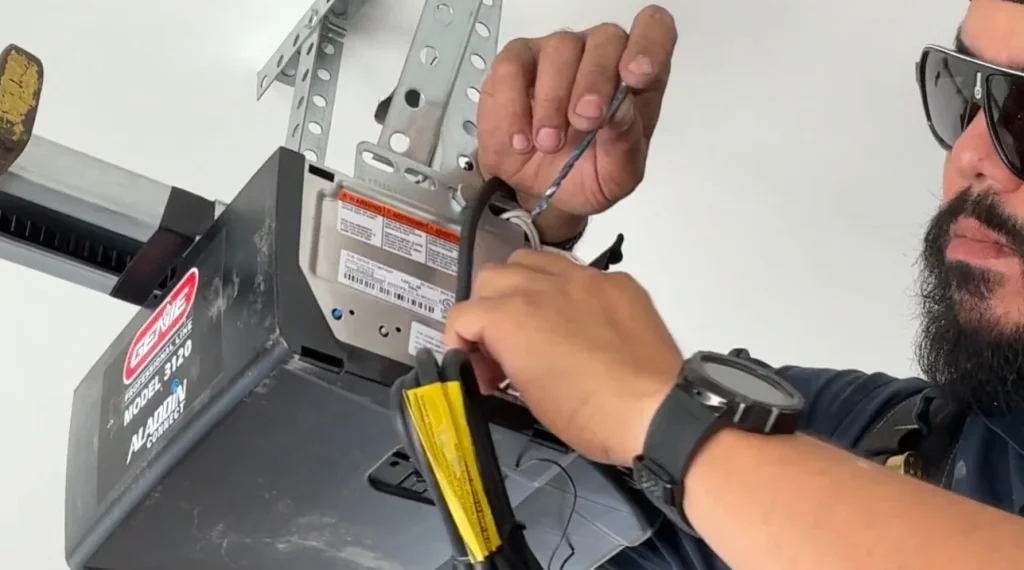 A close-up of a technician examining the wiring of a Genie model overhead motor unit, demonstrating professional troubleshooting for garage door opener problems.