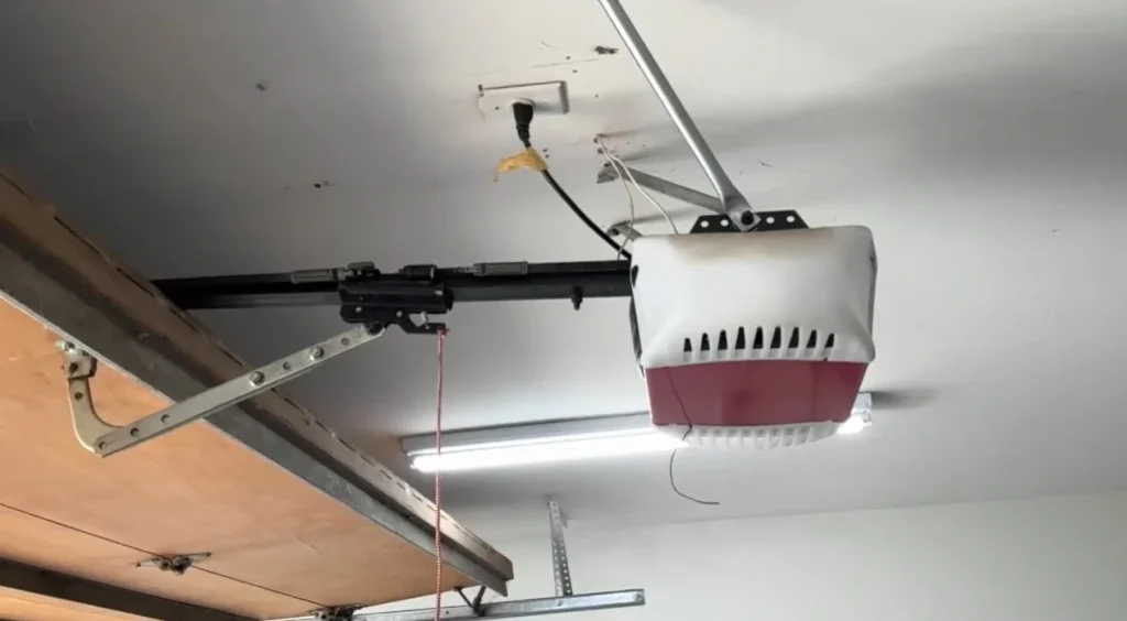 An overhead view of a ceiling-mounted garage door opener unit attached to its track system, indicating the equipment involved when you replace your garage door opener battery.