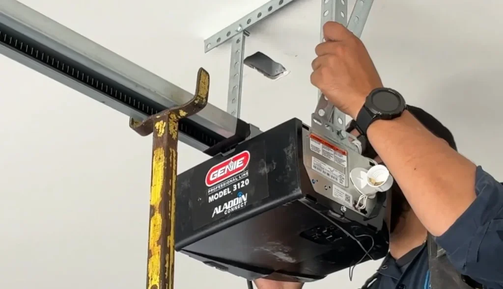 A professional technician mounting a Genie brand motor unit to the ceiling bracket, illustrating the installation of a new garage door opener.