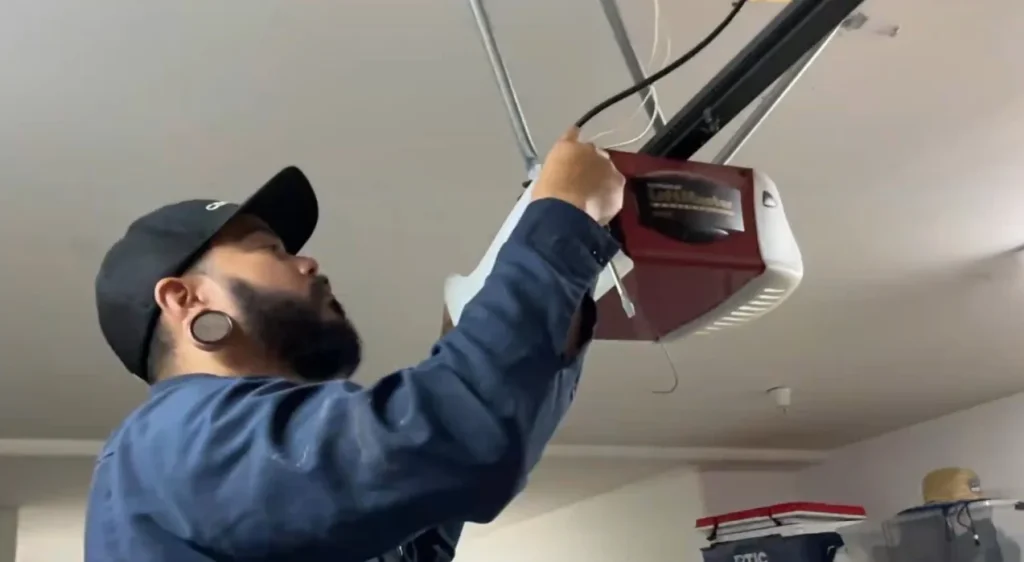 A close-up view of a technician adjusting the wiring and brackets of a ceiling-mounted LiftMaster motor unit, performing a professional garage door opener replacement.