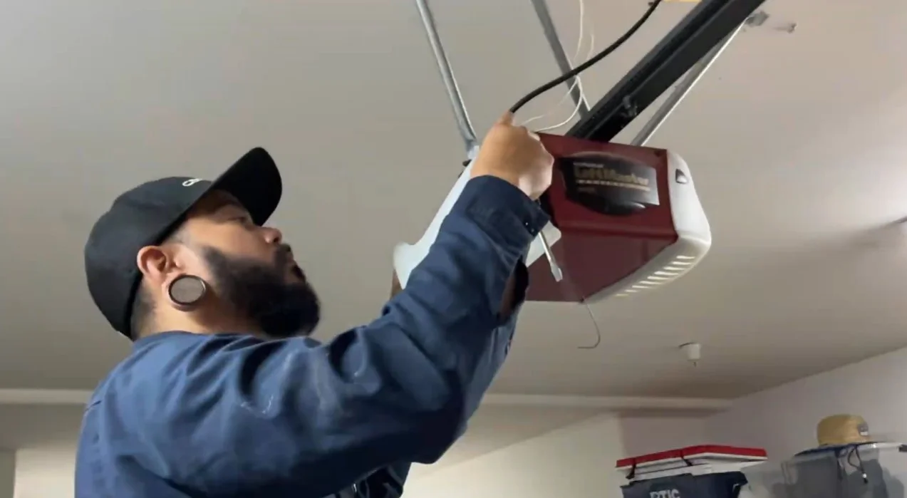 A close-up view of a technician adjusting the wiring and brackets of a ceiling-mounted LiftMaster motor unit, performing a professional garage door opener replacement.