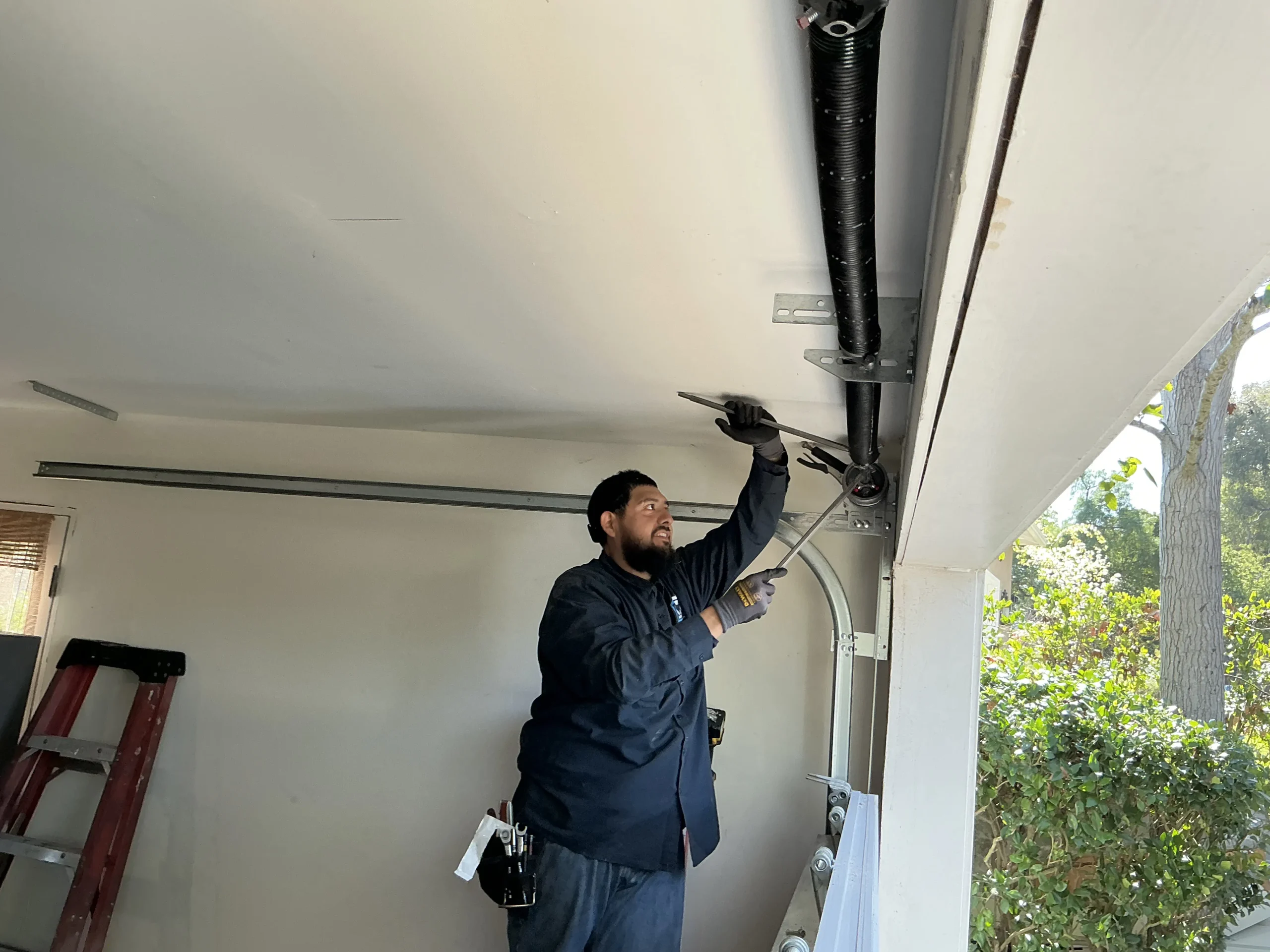 A professional technician using winding bars to tension a black overhead torsion spring, demonstrating reliable garage door spring repair near me.