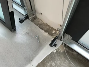 A close-up view of two black photo-eye units mounted near the garage floor tracks with loose screws nearby, indicating troubleshooting for safety sensor issues.