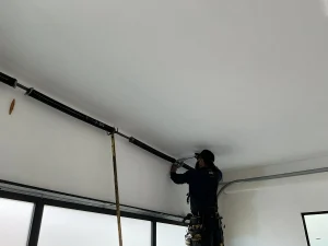A professional technician checking the overhead spring system, highlighting common signs your torsion spring needs replacement.