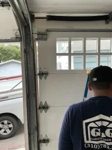 A technician examining an overhead garage door system, illustrating how to check for warning signs a torsion spring is failing.