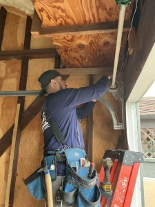 A technician with a tool belt working on the upper track assembly of a wooden garage structure to repair a broken garage door spring.