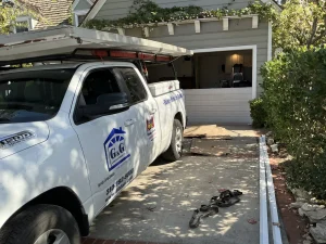 A white service truck parked in a driveway where track parts and tools are laid out to fix a system where the garage door gets stuck.