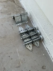 A collection of new galvanized steel brackets pre-assembled with smooth white nylon wheels sitting on a concrete garage floor, ready for a garage door roller replacement