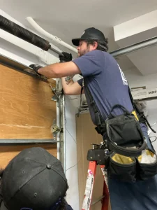 A skilled technician standing on a ladder to carefully adjust an overhead torsion spring, highlighting professional residential garage door spring repair.